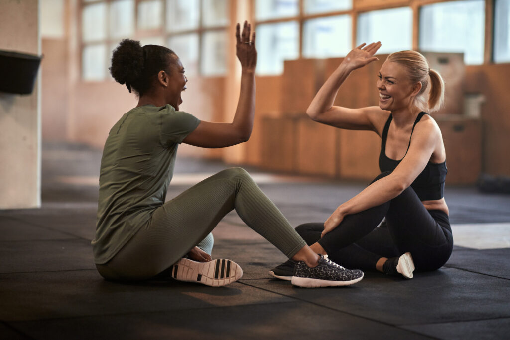 A veteran and a citizen being social laughing and high-fiving together while sitting on the gym floor after a workout